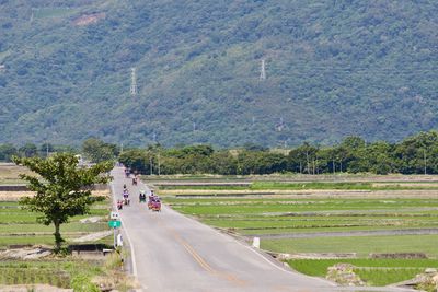 Vehicles on road amidst field against mountains