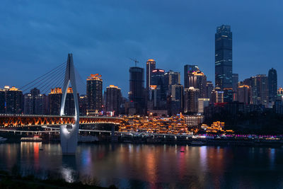 Illuminated buildings by river against sky in city