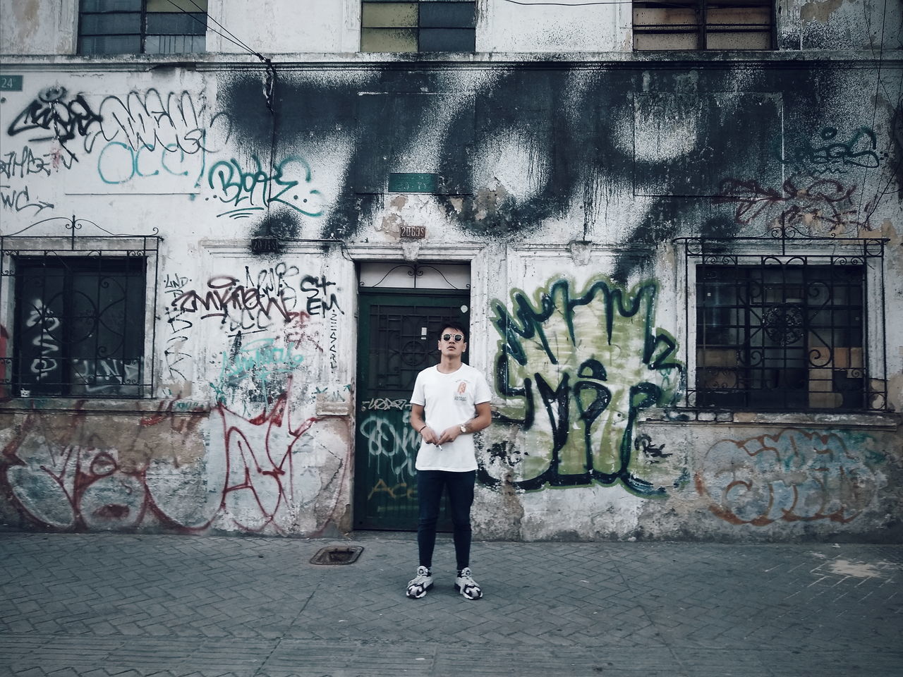 one person, full length, building exterior, architecture, graffiti, real people, built structure, looking at camera, portrait, standing, casual clothing, young adult, lifestyles, front view, day, city, wall - building feature, creativity, leisure activity, outdoors
