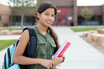 Young teen girl holding books in front of a school 