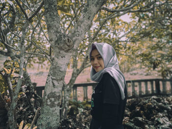 Portrait of young woman standing against plants