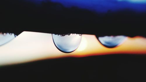 Close-up of water drop against sky during sunset