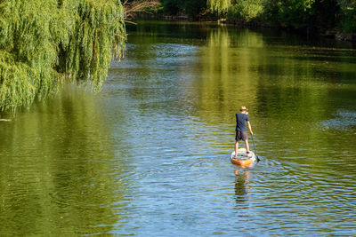 Rear view of man paddling on sup board on river.