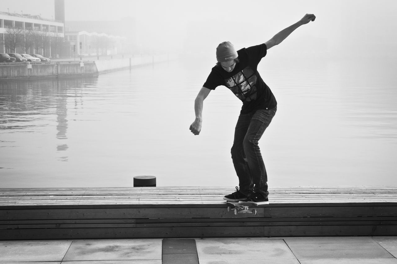 full length, lifestyles, leisure activity, water, young adult, casual clothing, jumping, standing, side view, arms outstretched, mid-air, person, balance, sunlight, young women, motion, built structure, reflection