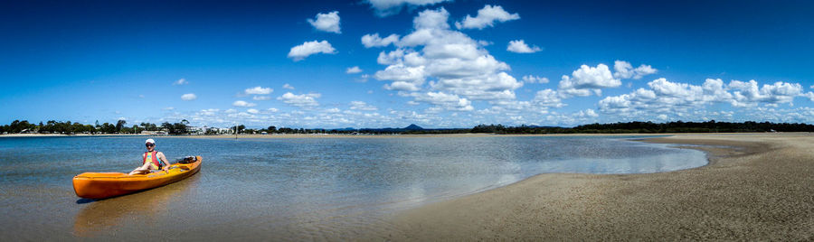 Panoramic view of woman sitting in kayak on sea shore against sky