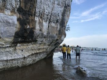 People on rock by sea against sky