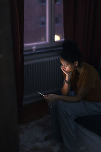 Young woman sitting on bed and using phone