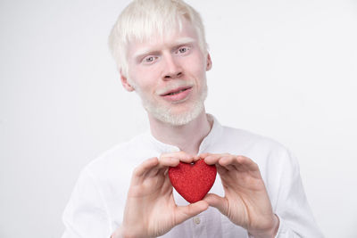 Portrait of man holding heart shape against white background