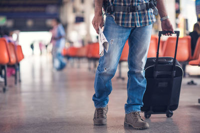 Low section of man with wheeled luggage walking at airport