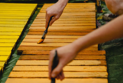 Cropped image of people painting wooden planks outdoors