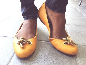 Low section of woman in yellow shoes standing on tiled floor