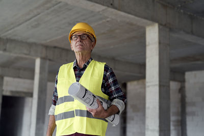 Thoughtful senior architect with blueprint at construction site