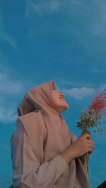 Low angle view of woman holding flower while standing against sky