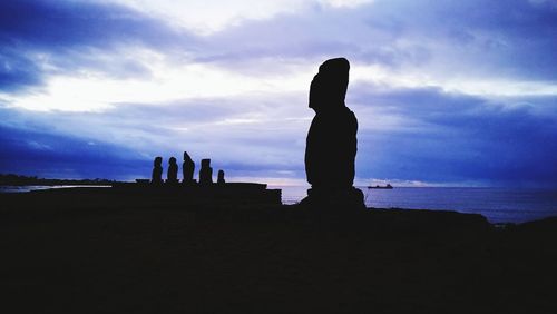 Silhouette man and woman standing by sea against sky during sunset