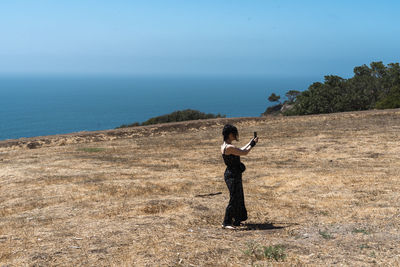 Rear view of woman jumping on mountain against sky