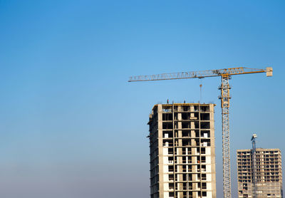 Low angle view of crane by building against clear blue sky