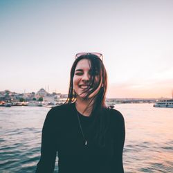 Portrait of smiling young woman standing in sea against sky