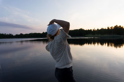 Rear view of woman standing by lake against sky during sunset