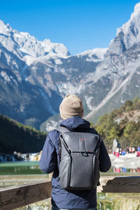 Rear view of man wearing backpack while standing against mountains during winter