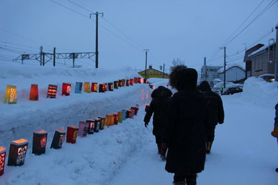 Rear view of people walking on snow covered field against sky