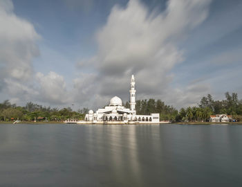 View of building by lake against cloudy sky