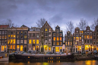 Illuminated buildings by canal against sky in city