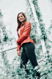 Portrait of smiling young woman standing against wall