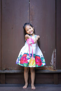 Full length portrait of smiling girl standing against wall