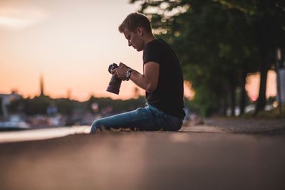 Side view of man sitting with camera in city