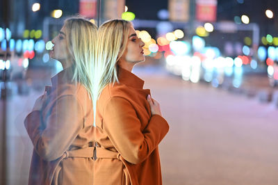 Side view of young woman standing on street at night