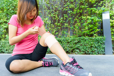 Full length of young woman applying adhesive bandage on leg