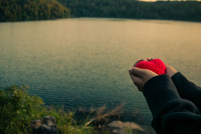 Cropped hands holding woolen red heart at lakeshore