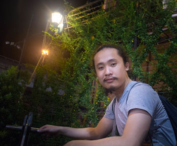 Portrait of young man sitting by plants at night