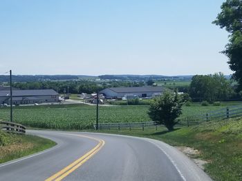 Road leading towards city against clear sky