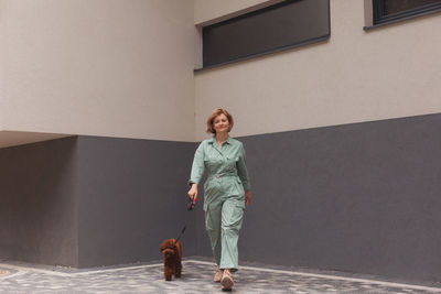 Full length of woman walking with dog against wall