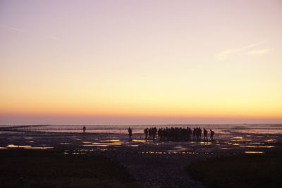 Silhouette people on beach against clear sky during sunset