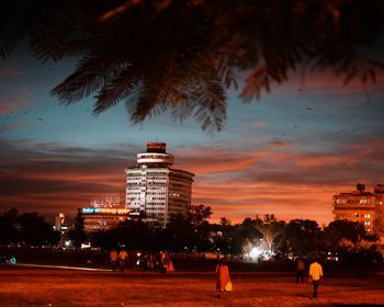 People by illuminated buildings against sky at night