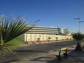 Road by buildings in city against clear sky