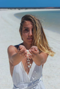 Young blonde woman with beautiful hands holding and releasing small shells on paradisiacal beach