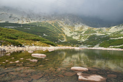 Scenic view of skalnate pleso lake against mountains in foggy weather