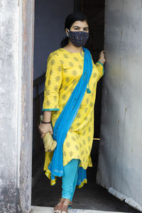 An indian woman in yellow dress and face mask on is going outside during corona virus pandemic