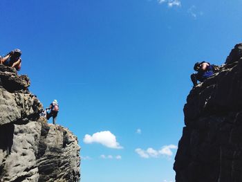 Low angle view of people on rock against blue sky