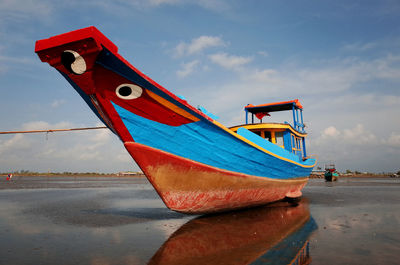 Red boat moored on beach against sky