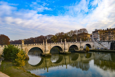 Arch bridge over river by buildings against sky