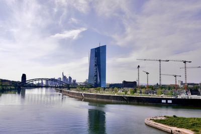 Bridge over river by buildings against sky with the ecb in the foreground 