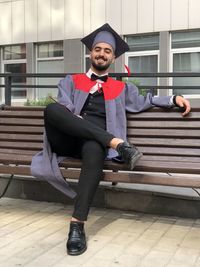 Smiling graduated young man sitting on bench