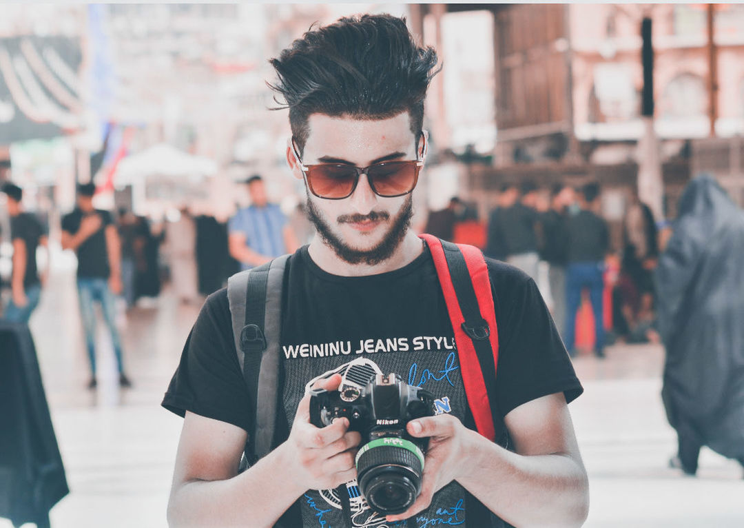 one person, focus on foreground, photography themes, young adult, young men, front view, holding, casual clothing, real people, portrait, camera - photographic equipment, photographic equipment, incidental people, communication, technology, text, leisure activity, glasses, waist up, digital camera, photographer