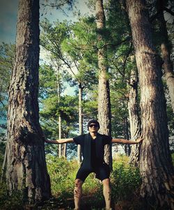 Portrait of young man standing by tree trunk in forest