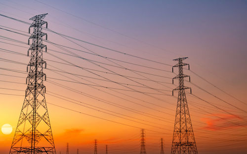 Low angle view of electricity pylon against sky during sunset.