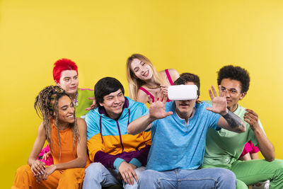 Full length portrait of smiling young couple sitting on yellow wall